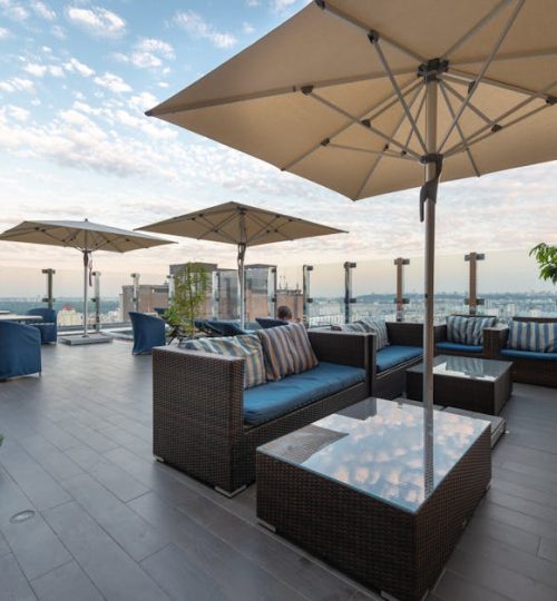 Modern lounge zone with comfortable sofas and tables under umbrellas on terrace in daytime